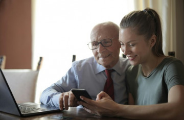 positiver-alterer-mann-und-lachelnde-junge-frau-die-smartphone-beim-sitzen-am-tisch-beobachten