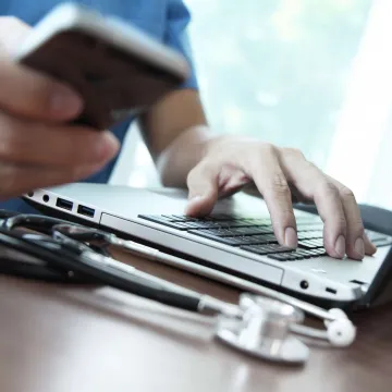 Hand am Laptop und andere Hand mit Handy