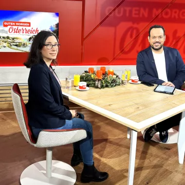 Moderator sitzt mit Interviewpartnerin am Tisch