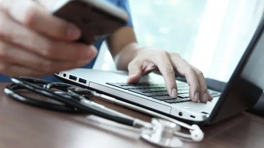 Hand am Laptop und andere Hand mit Handy